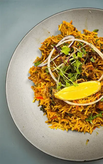 Biryani on a plate with a lemon wedge and microgreens