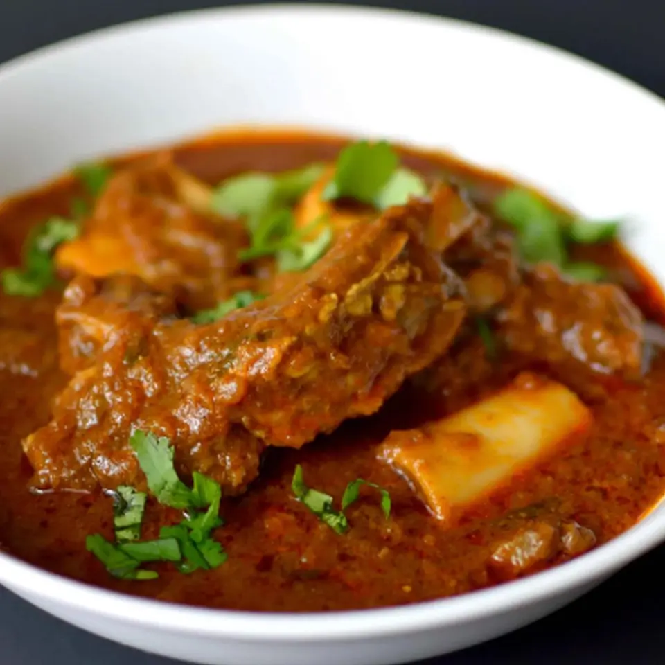 Goat curry in a white bowl topped with coriander